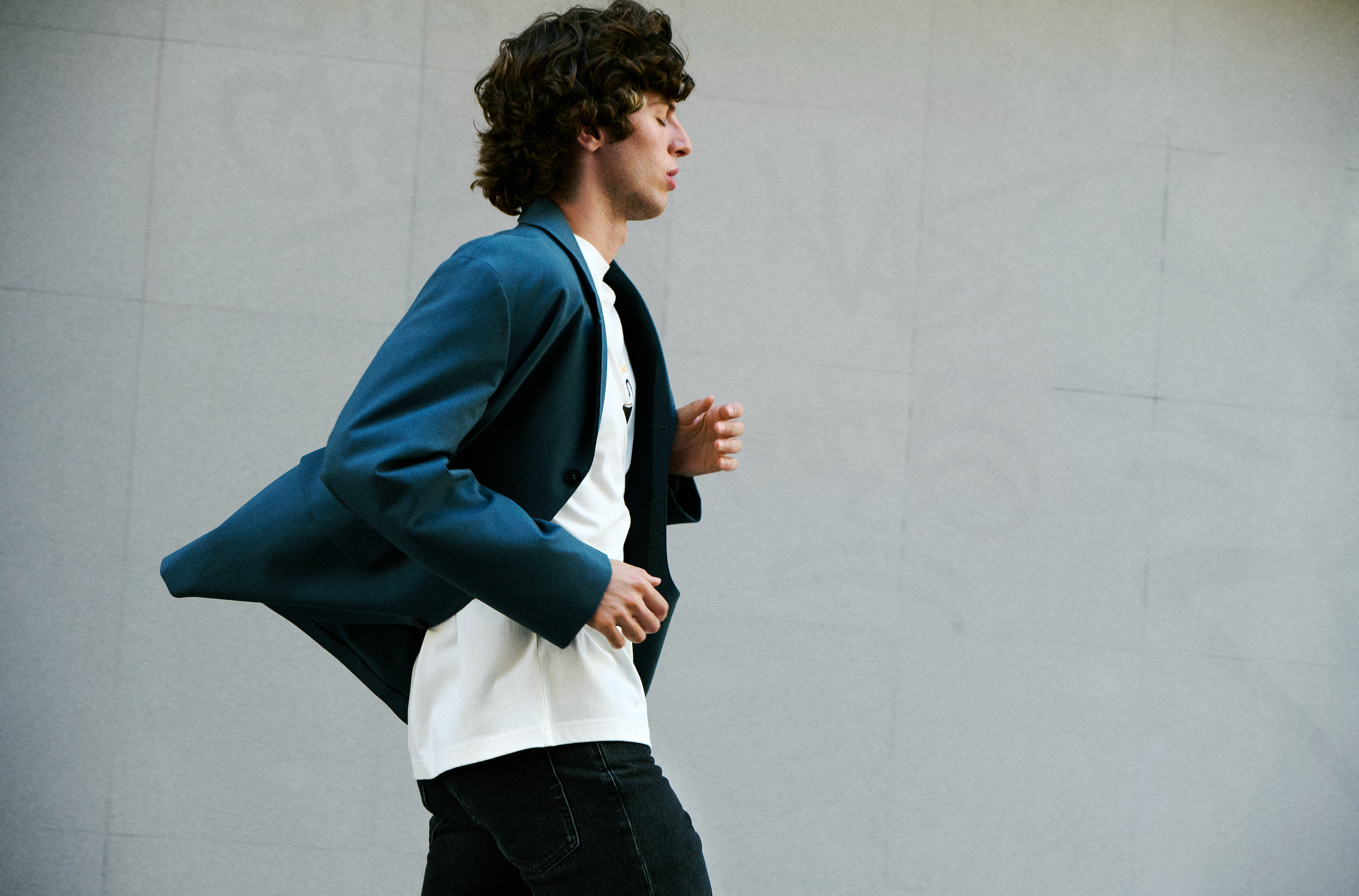 Selected menswear navy blazer styled with white t-shirt and black jeans, worn by a model in motion